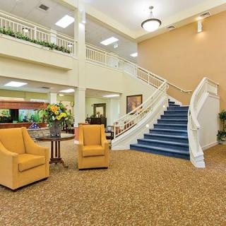 A spacious and elegantly designed lobby with a staircase, comfortable chairs, and a carpeted floor.