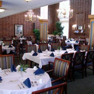 An elegant dining room with neatly arranged tables and chairs, featuring white tablecloths and blue napkins.