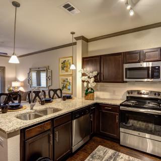 A modern kitchen with dark cabinets, stainless steel appliances, and elegant pendant lighting.