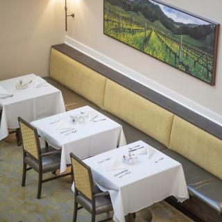 An empty restaurant dining area with neatly set tables and a landscape painting on the wall.