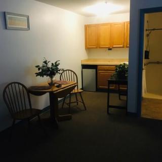 A cozy kitchen and dining area with wooden cabinets, a small table, and chairs. Two potted plants add a touch of greenery to the space.