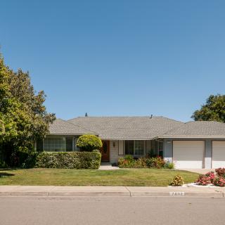 A suburban single-story house with a well-maintained lawn and surrounding trees.