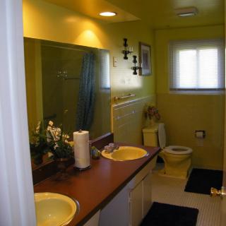 A bathroom with yellow walls featuring a double sink, a mirror, and a window.