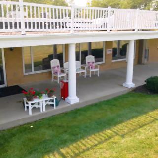 A well-maintained outdoor patio area with chairs, a table, and columns, overlooking a green lawn.