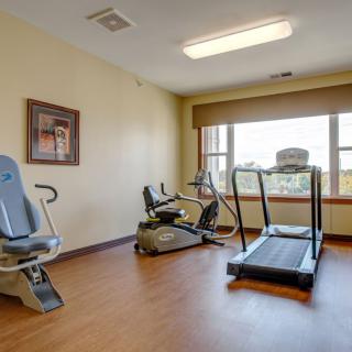 A small gym with fitness equipment, including a treadmill and stationary bike, located in a well-lit room with a large window.