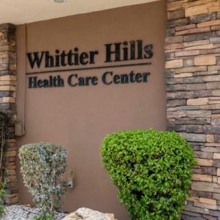 Entrance sign of Whittier Hills Health Care Center surrounded by landscaping.