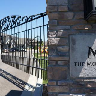 Entrance to a gated community with an ornamental iron gate and stone wall.
