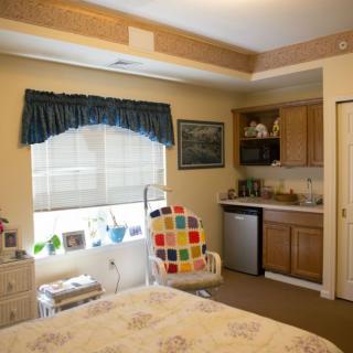 A cozy bedroom with a small kitchenette and a colorful chair by the window.