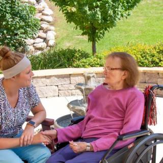 A caregiver and an elderly woman in a wheelchair enjoying time together outdoors.