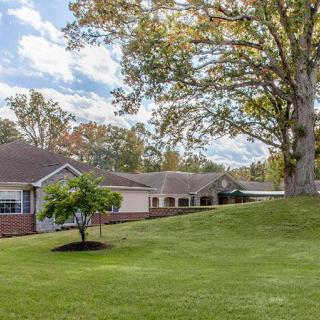 A picturesque view of a building surrounded by trees and a well-manicured lawn under a blue sky.