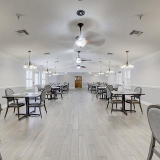 A spacious dining area with multiple tables and chairs, featuring bright lighting and ceiling fans.