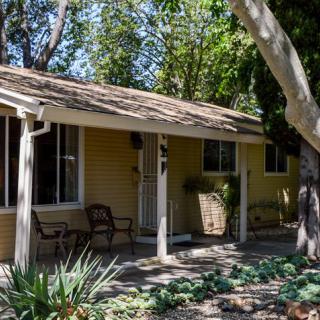 A small house with a porch surrounded by trees and a garden.