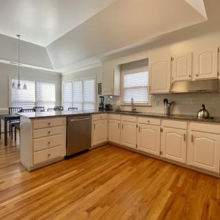 A spacious kitchen with white cabinets, stainless steel appliances, and hardwood flooring.