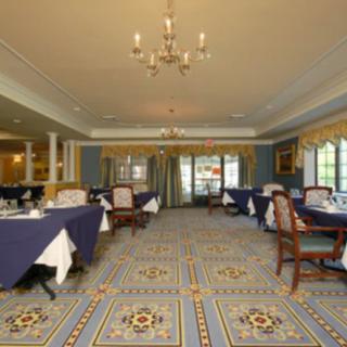 A spacious and elegantly decorated dining area with neatly arranged tables and chairs, featuring a patterned carpet and a chandelier.