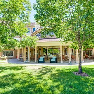A sunny day view of a building with a covered patio, surrounded by green trees and a well-maintained lawn.