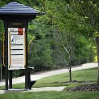 An information board stands next to a pathway in a lush, green park.