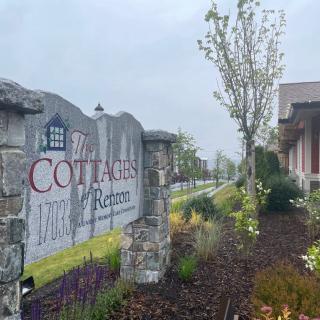 A stone sign for 'Cottages' with well-maintained landscaping and trees on an overcast day.