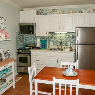 A modern kitchen and dining area featuring white cabinets, stainless steel appliances, a wooden table with chairs, and stylish decor.