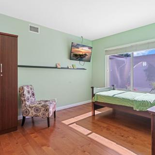 A cozy bedroom with a single bed, green walls, wooden flooring, a floral chair, and a mounted television.