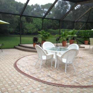 A screened-in patio area with a glass table surrounded by white chairs, featuring potted plants and a view of the garden.