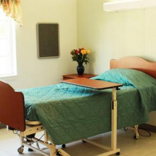 An empty hospital room with a single bed, side table with flowers, and a window for natural light.