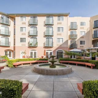 A sunny courtyard with a central fountain surrounded by benches and a modern apartment building.