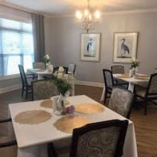 A cozy, elegantly decorated dining room with several tables and chairs, adorned with flowers and artwork on the walls.