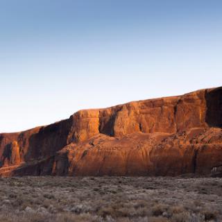 A stunning view of a rock formation illuminated by the warm hues of sunset in a vast desert landscape.