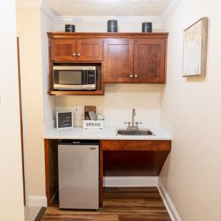 A compact kitchenette featuring a microwave, a mini refrigerator, and a small sink with overhead cabinets.