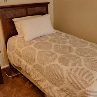 A neatly made single bed with a patterned quilt and pillow in a bedroom.
