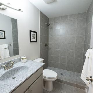 A modern bathroom featuring a walk-in shower, sink, and toilet with gray tiles.