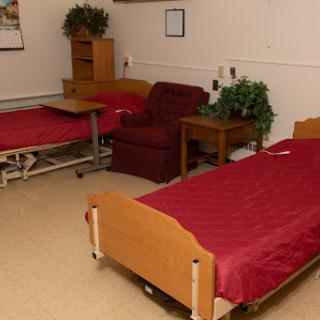 A simple hospital room featuring two beds, a reclining chair, and a small table.