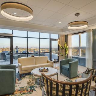 A modern living room with large windows offering a city view, featuring comfortable seating and stylish lighting fixtures.