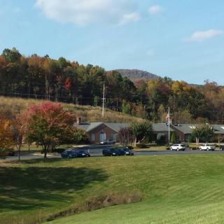 A scenic countryside view with colorful autumn trees, a building, and cars parked on a grassy field.