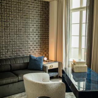 A modern living room featuring a sectional sofa, geometric wallpaper, and ample natural light from large windows.