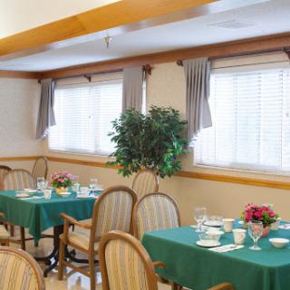 A cozy dining area featuring green tables, wooden chairs, and decorative plants.
