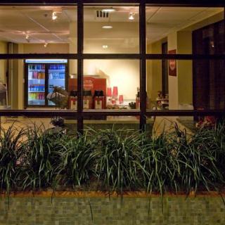A nighttime view of a cozy lobby area through a glass window, showcasing modern furniture and greenery.