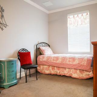 A cozy bedroom with a single bed and pink bedding, accompanied by a decorative chair and side table near the window.