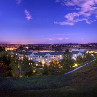 A view of a suburban area at dusk, with lights illuminating the buildings under a colorful sky.