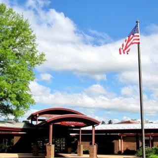 A school building with a U.S. flag flying outside under a partly cloudy sky.