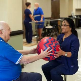 A healthcare professional assists a patient with an exercise routine using a large ball during a physical therapy session.