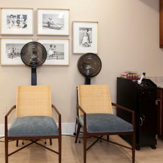 A cozy corner featuring two stylish chairs, framed artwork on the walls, and standing fans for comfort.