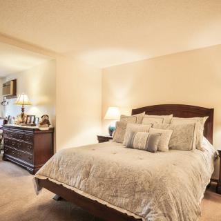 A cozy bedroom with a neatly made bed, elegant lamps, and polished furniture.