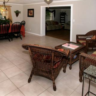 A cozy living room with wicker furniture and a dining area, featuring tile flooring and home decor.