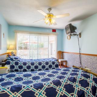A cozy bedroom with twin beds, blue bedspreads, a ceiling fan, and natural light streaming through a large window.