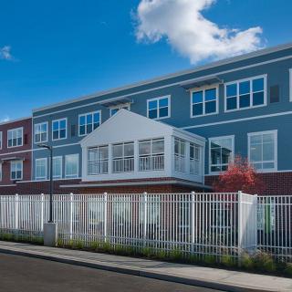 A modern residential apartment building with a white fence and a bright blue sky.