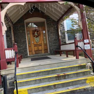 A building entrance with stone walls, featuring steps leading up to a door adorned with a wreath.