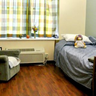 A cozy bedroom with a bed, armchair, and a window with checkered curtains.