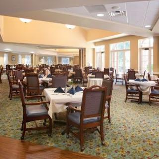 An elegant dining room with several tables and chairs neatly arranged, featuring a carpeted floor and ample natural light.
