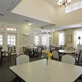 A spacious dining room with neatly arranged tables and chairs, featuring a vase of flowers on the table and a chandelier overhead.